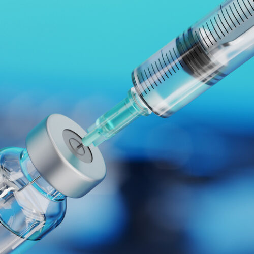 Medical disposable syringe for vaccine injection and glass vial on blue blur background.